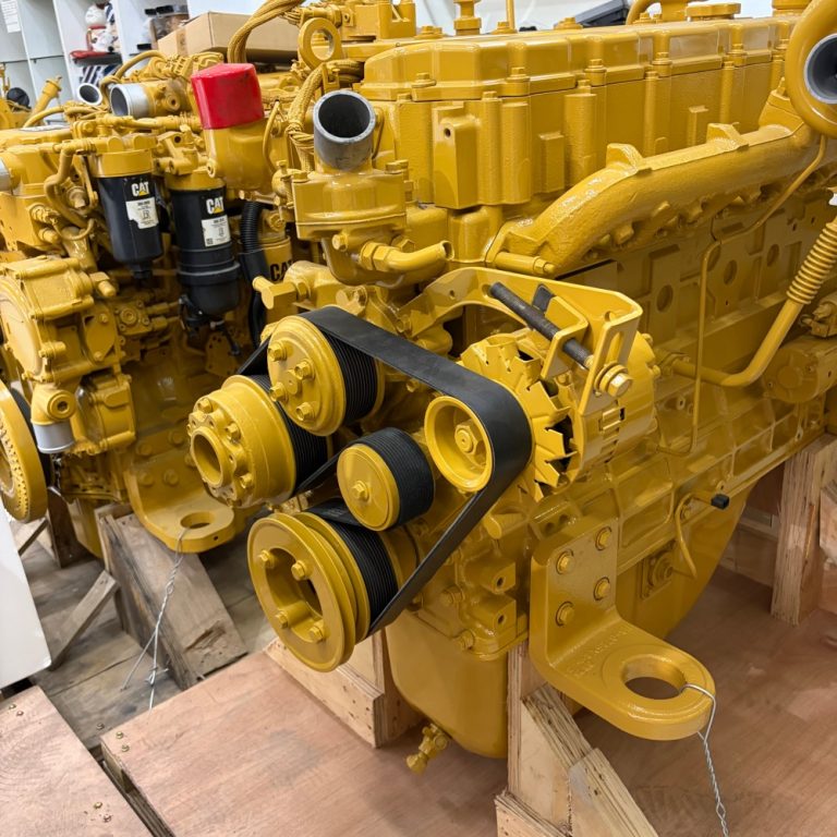 Yellow excavator diesel engine assembly with belts, filters, manifolds and mounting points visible